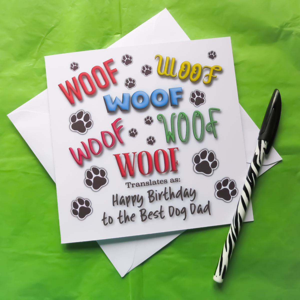“Square best dog dad birthday card
with a white envelope, laid on a green background.