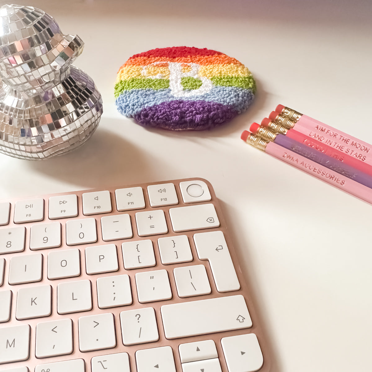Bright rainbow mug rug surrounded by stationery, keyboard and a mirrored duck – colourful desk decor idea.