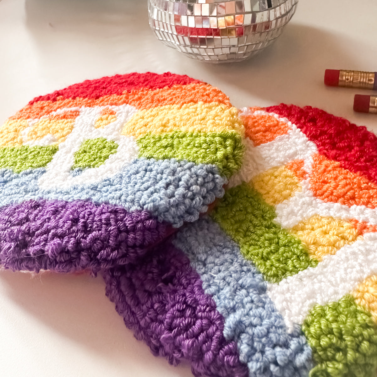 Stacked handmade rainbow mug rugs – round punch needle coasters made in UK using soft yarn.