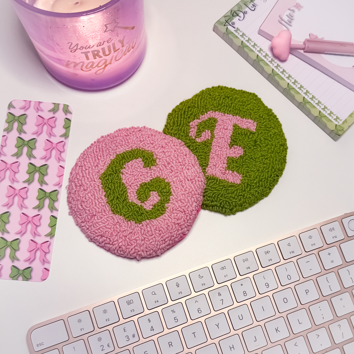 Two round textured coasters with letters 'G' and 'E', a pink candle, and a keyboard on a white surface.