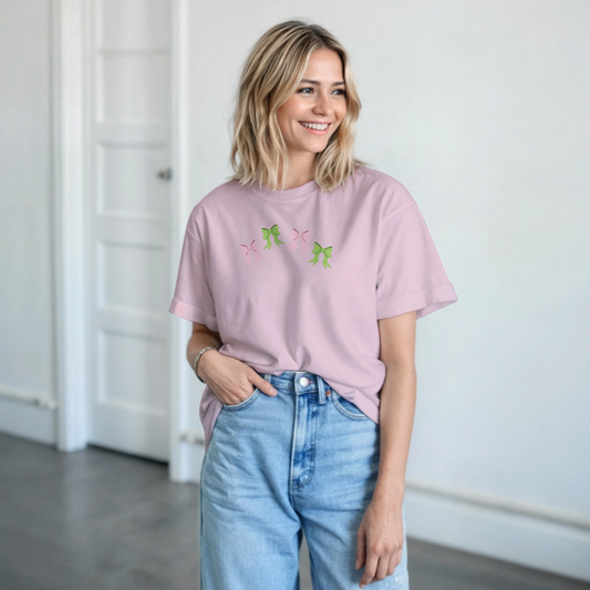 A blonde female wearing Pink bows and green bows design on pastel pink tee