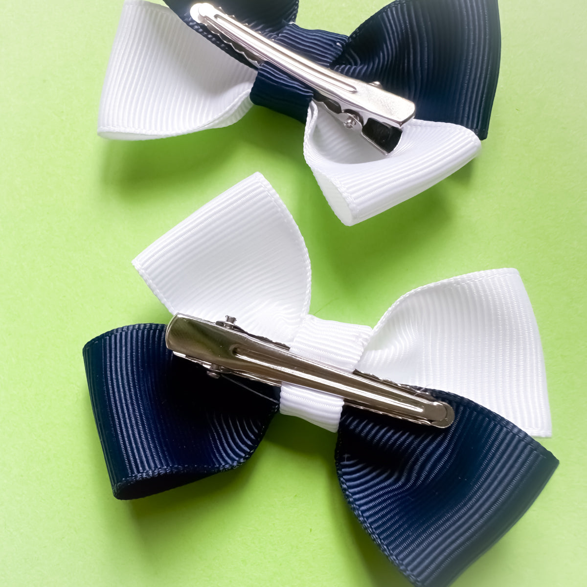 Two hair bows with alligator clips on a green background
