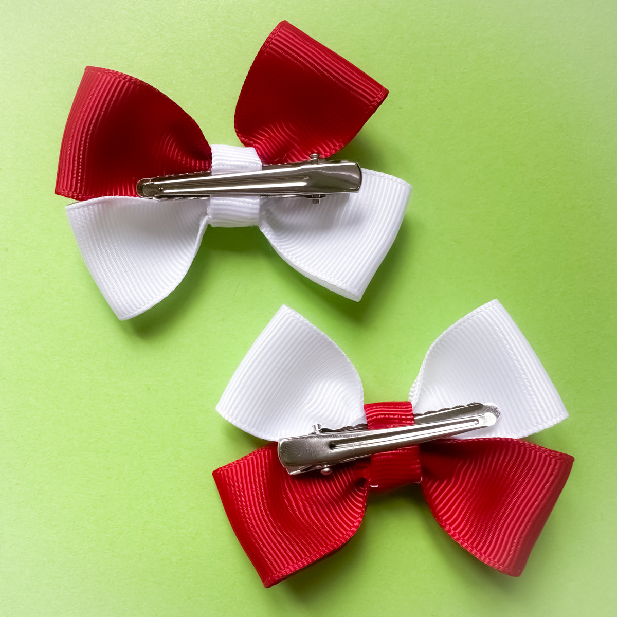 Two red and white hair bows with alligator clips on a green background