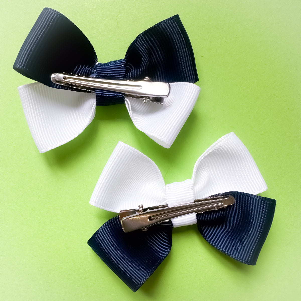 Two hair bows with metal alligator clips on a green background