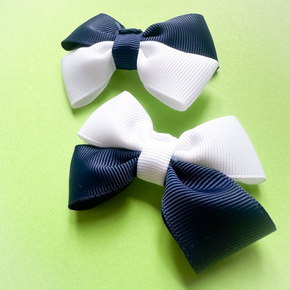 Two navy and white hair bows on a green background