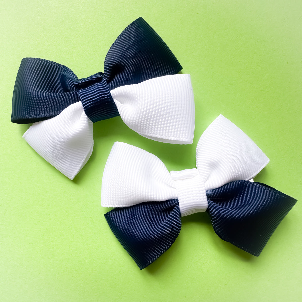 Two navy and white hair bows on a green background for football match days and World Cup celebrations.