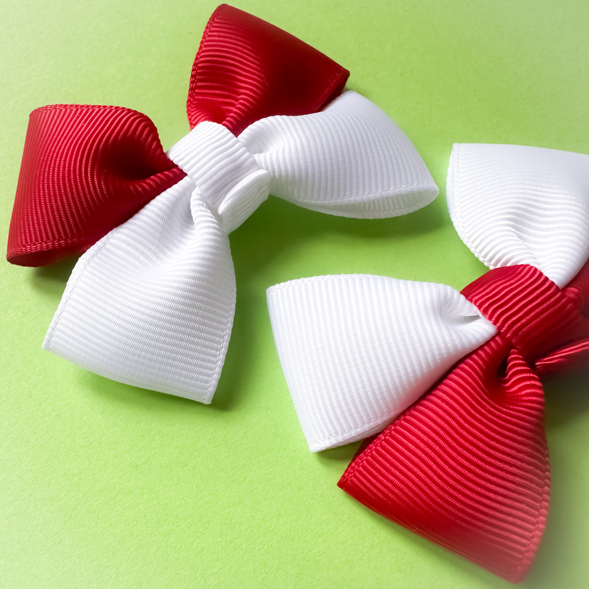 Close up of two red and white hair bows on a green background