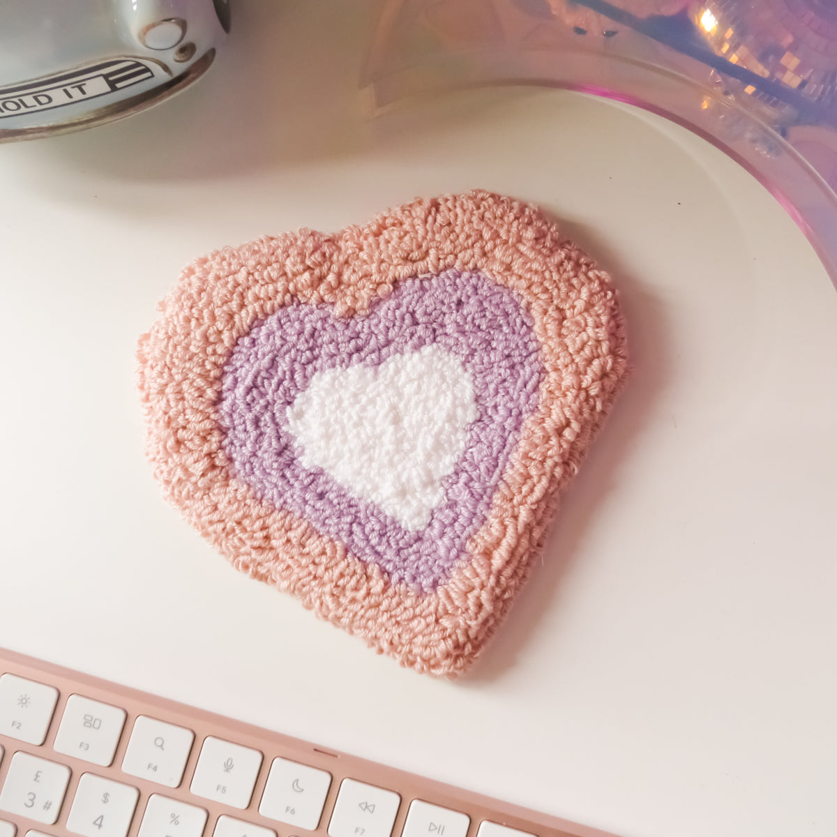 Heart-shaped pink and purple textured coaster on a white surface with a keyboard in the foreground.
