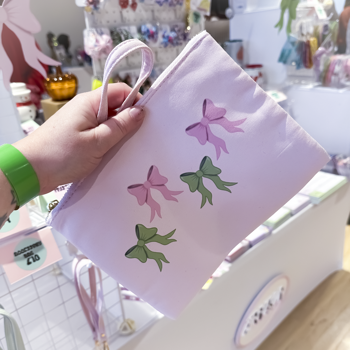 Pink accessory bag with green bow pattern, clutch-style zipper pouch