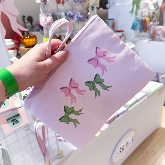 Pink accessory bag with green bow pattern, clutch-style zipper pouch