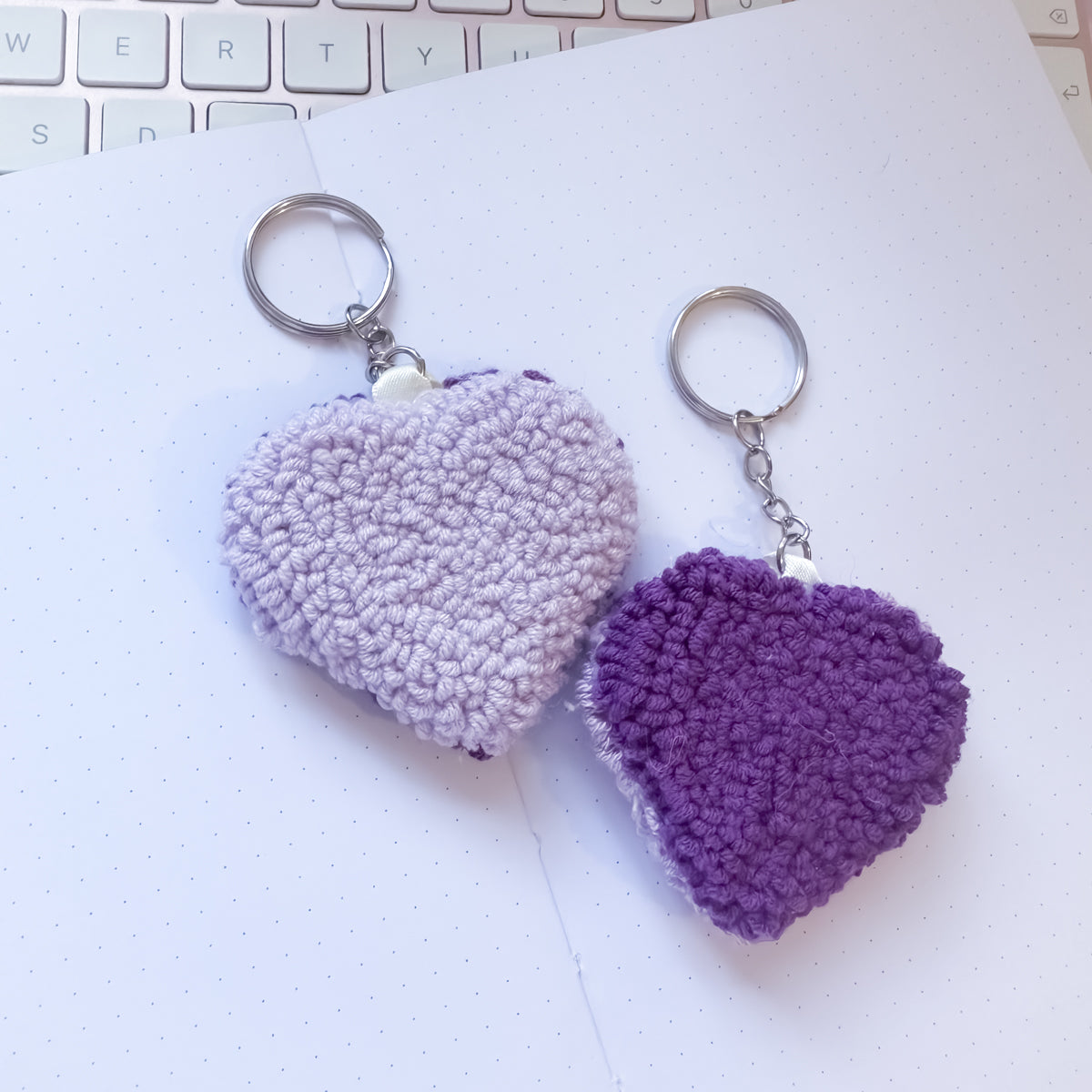 Two heart-shaped keychains, one light purple and one dark purple, on a white surface with a keyboard in the background.