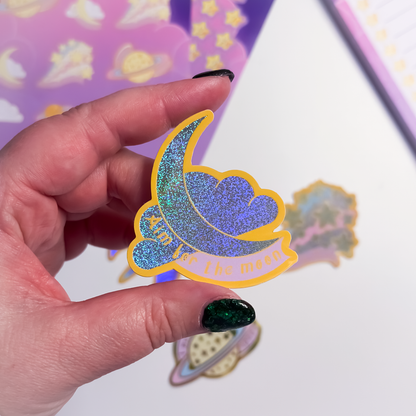 Hand holding a glittery sticker with a moon and star design against a colorful background
