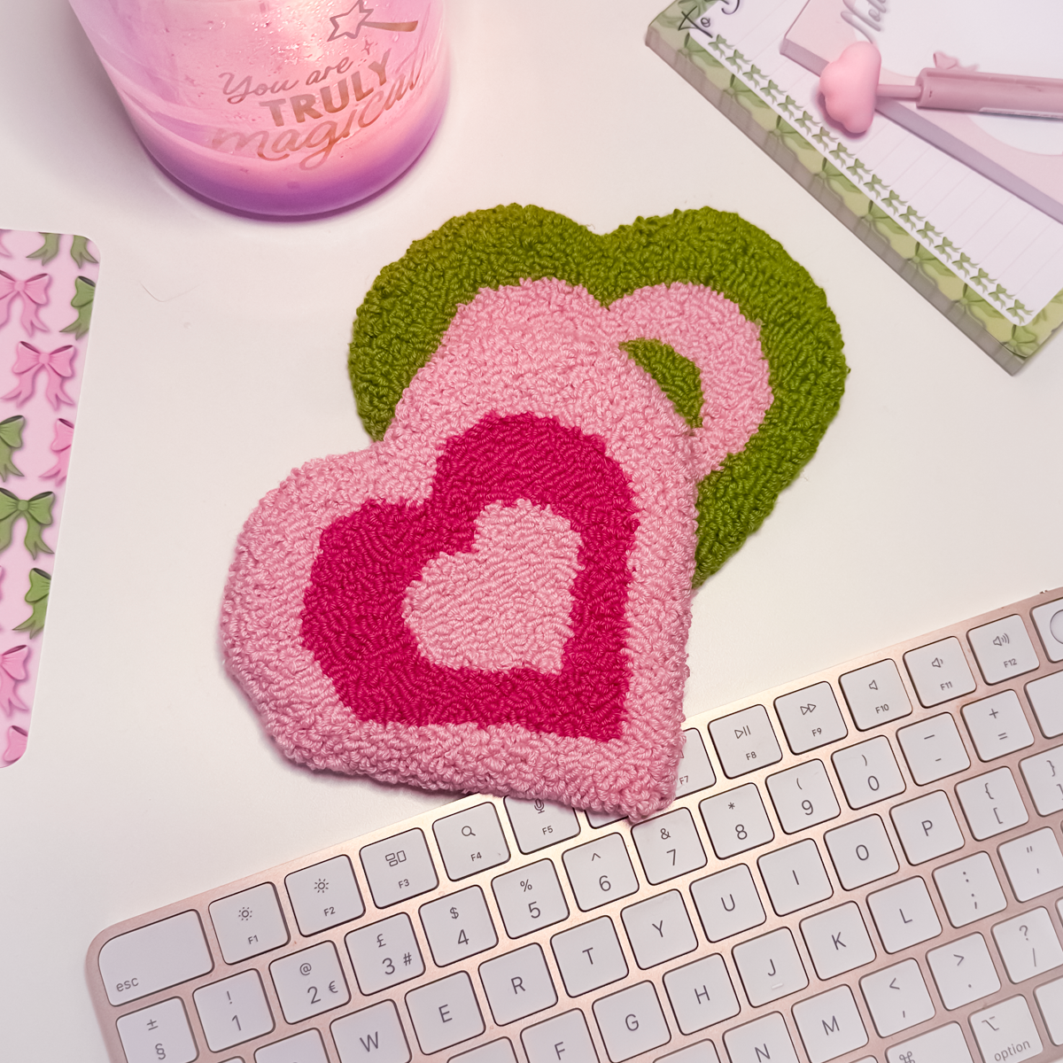 Heart-shaped pink and green coasters on a keyboard with a lilac candle in the background.