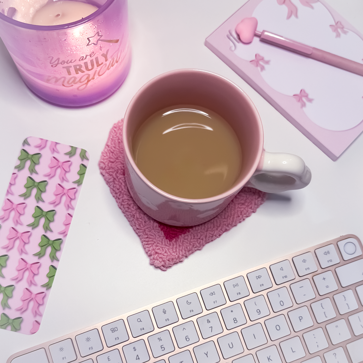 Pink mug with tea on a pink heart shaped mug rug with a keyboard and decorative items.
