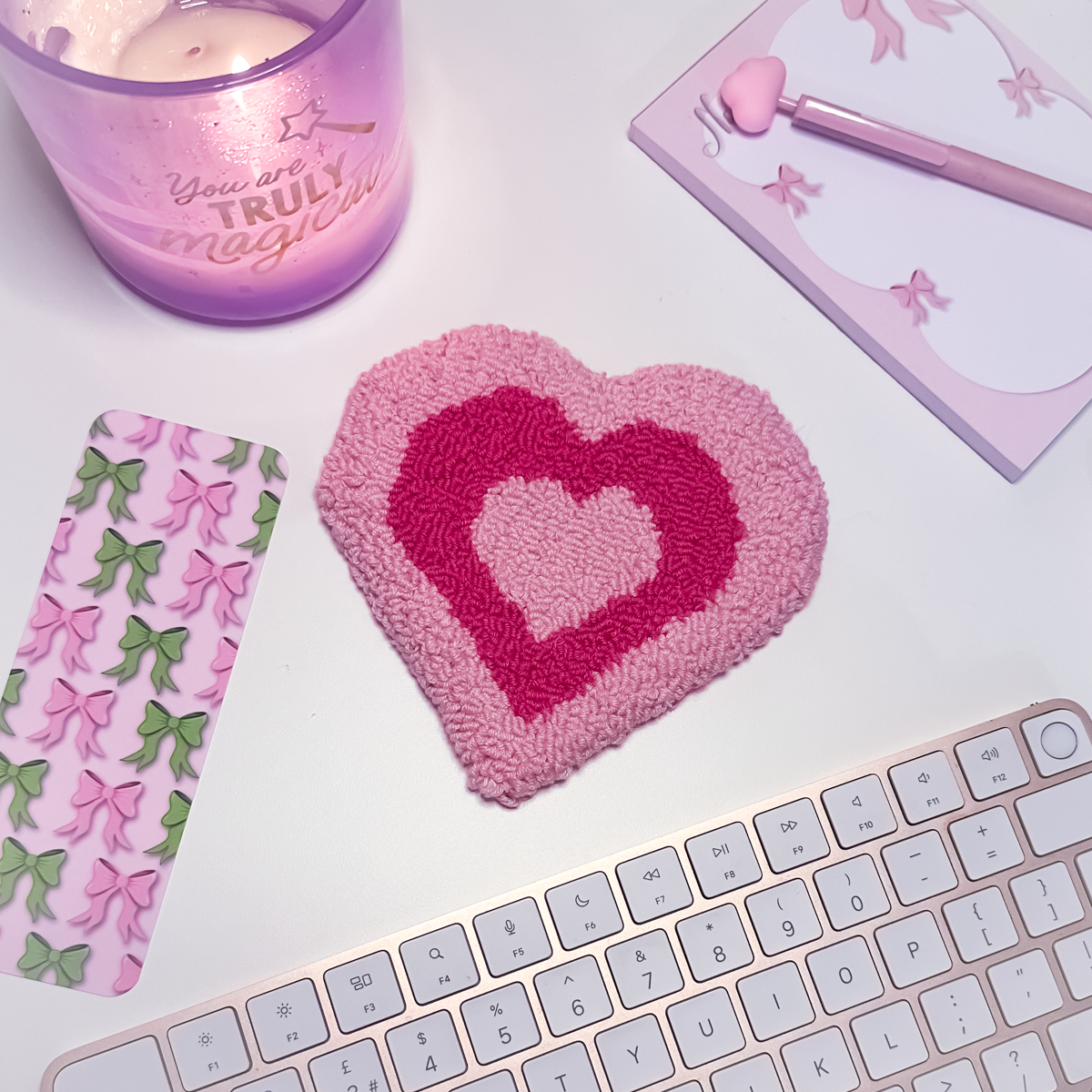 Heart-shaped pink mug rug with a candle, notebook, and keyboard.