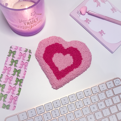 Heart-shaped pink mug rug with a candle, notebook, and keyboard.