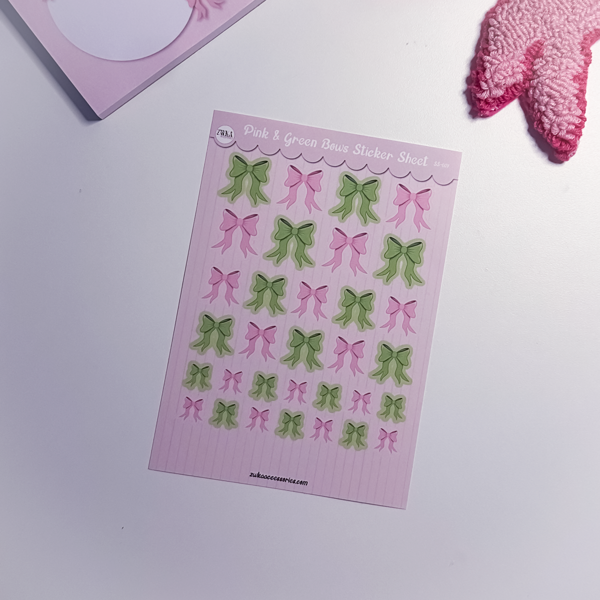 Sheet of pink and green bow stickers on a white surface with a pink object partially visible.