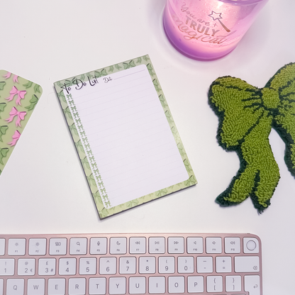 Green Bows To Do List A6Notepad with decorative green bows border, pink keyboard, and green bow mug rug on a white surface