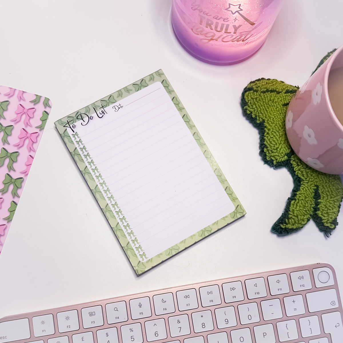 Notepad with a green border, pink mug, and keyboard on a white surface