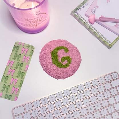 Pink textured coaster with green letter 'G', candle, and keyboard on a light surface