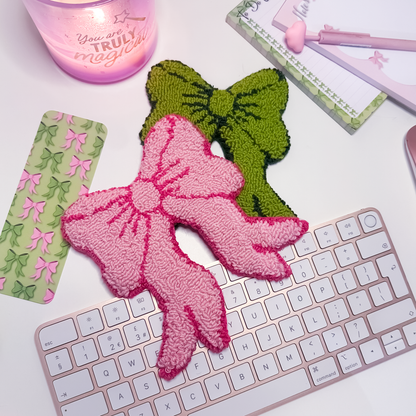 Pink and green bow-shaped mug rugs on a keyboard with a pink candle and decorative box in the background.
