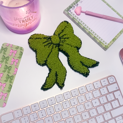 Green bow-shaped mug rug on a desk with a keyboard, notebook, and candle.