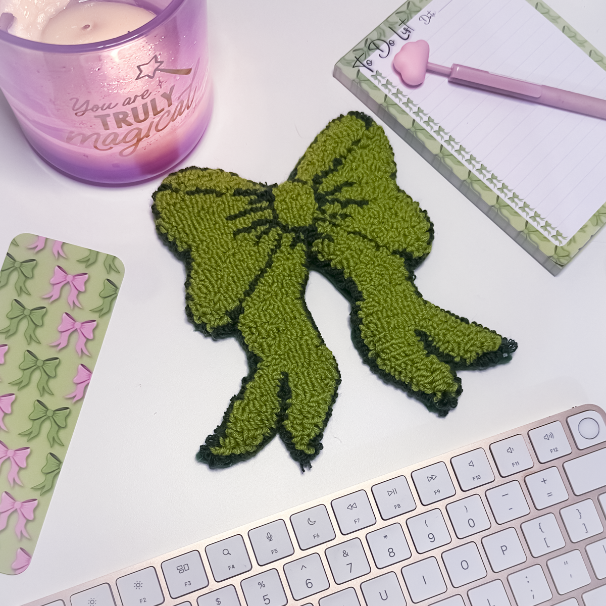 Green bow mug rug on a desk with a pink candle and stationery items.