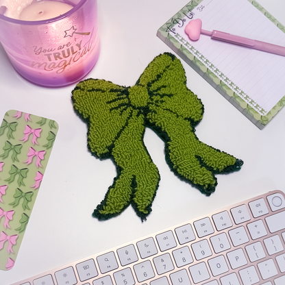 Green bow mug rug on a desk with a pink candle and stationery items.