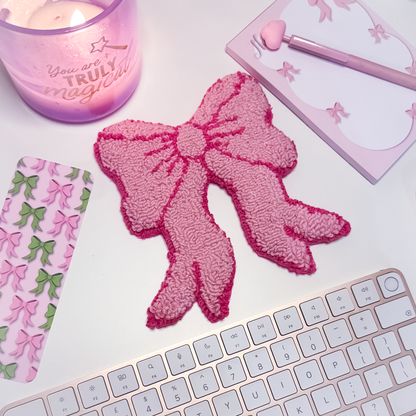 Pink bow mug rug on a white surface with a candle, notebook, and keyboard.