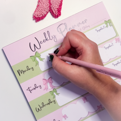 Pink and green Weekly planner with hand writing on it, pink pen visible