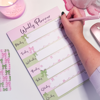 A4 weekly planner notepad with pink and green bow design, Monday to Sunday layout and tick circles for tasks with a hand writing on it