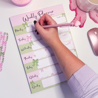 Weekly planner with decorative elements on a desk with a pink pen